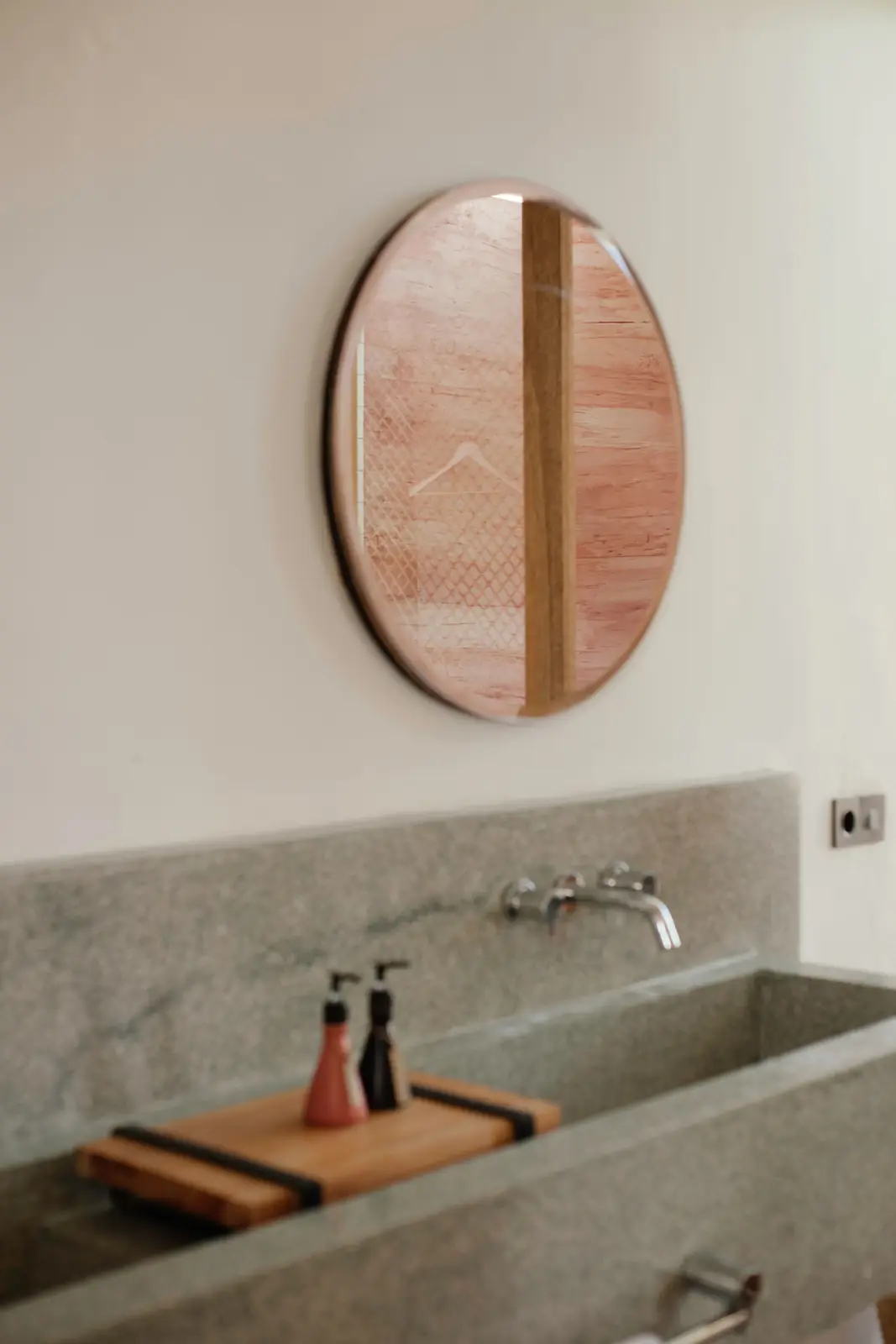 A sleek minimalist bathroom featuring a modern oval mirror and stone sink.