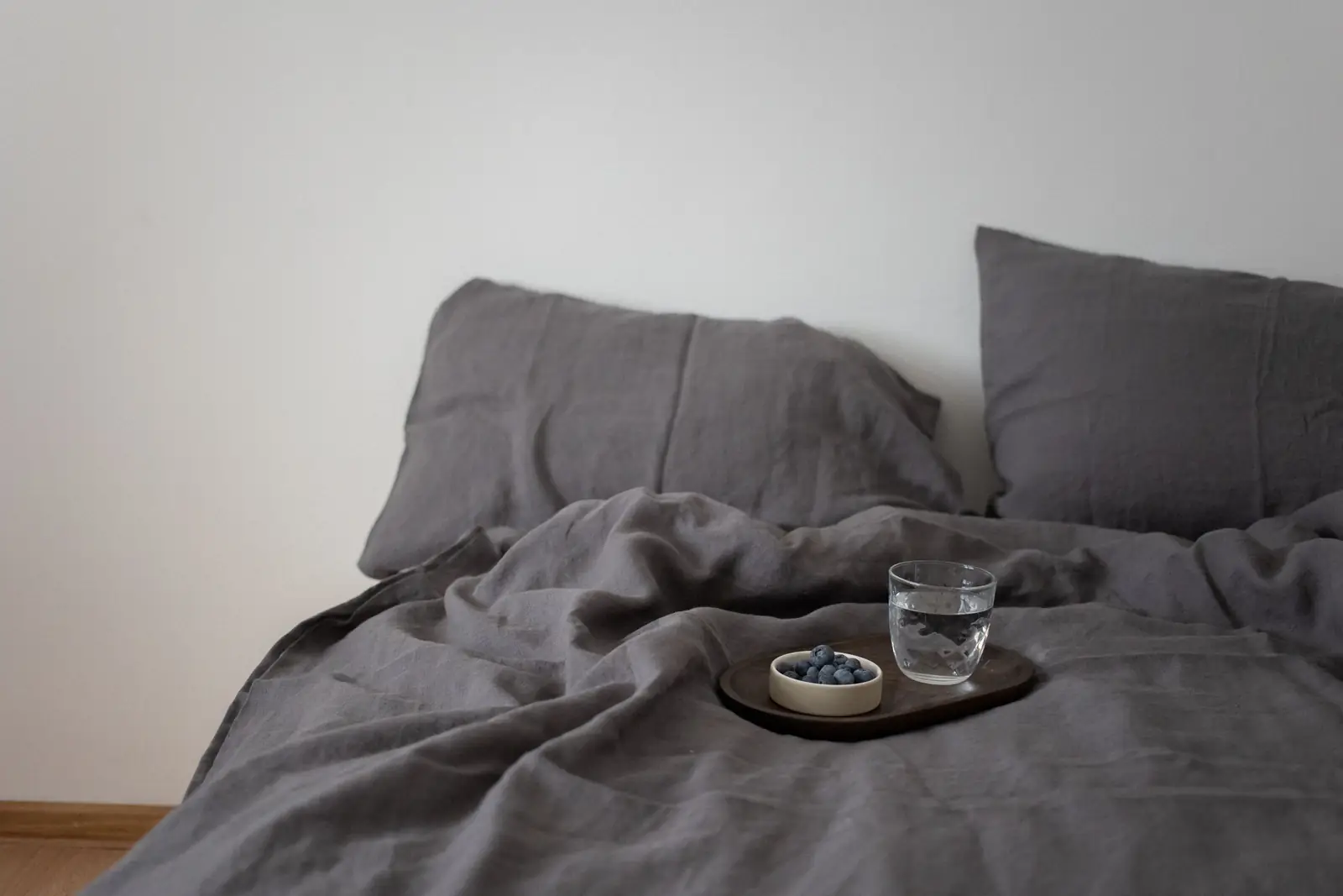 Minimalist bedroom with grey linen bedding, blueberries, and a glass of water on a tray.