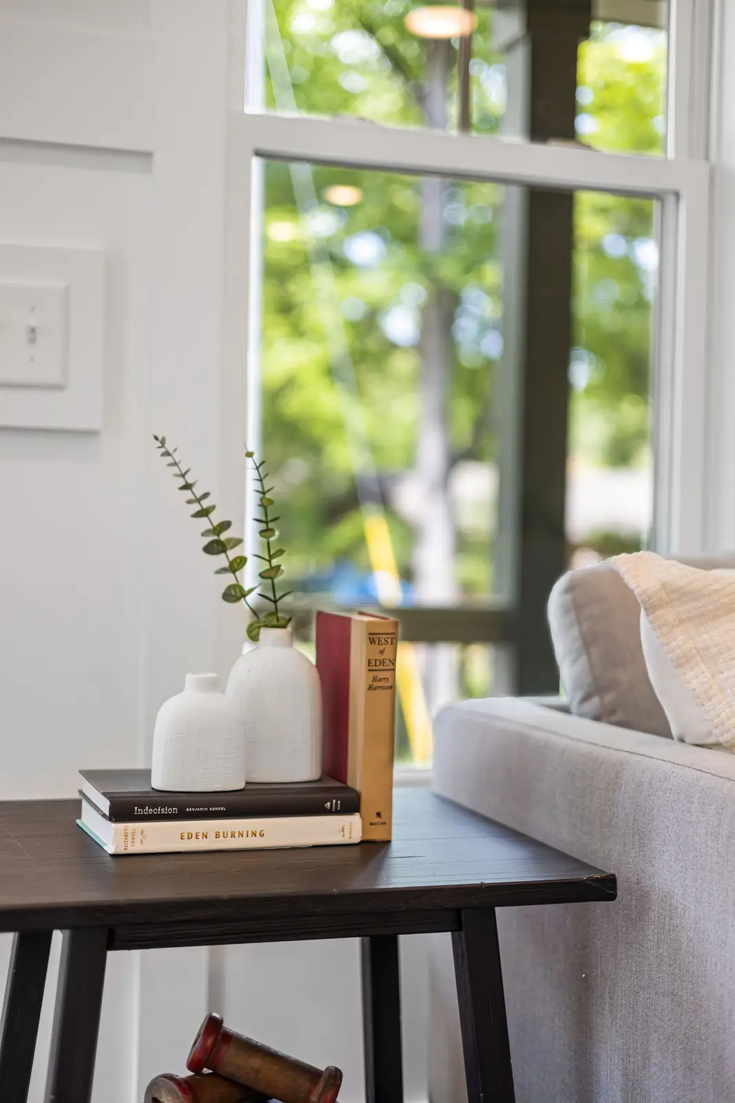 Stylish living room setup with books and vases on a wooden table by the window.